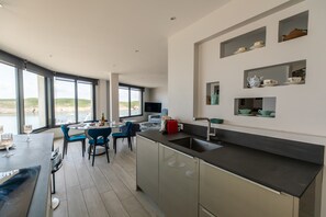 A modern kitchen with a dining area, large windows, and a view of the sea. - Panoramic Sea-view Apartment in Le Conquet (Le Conquet)