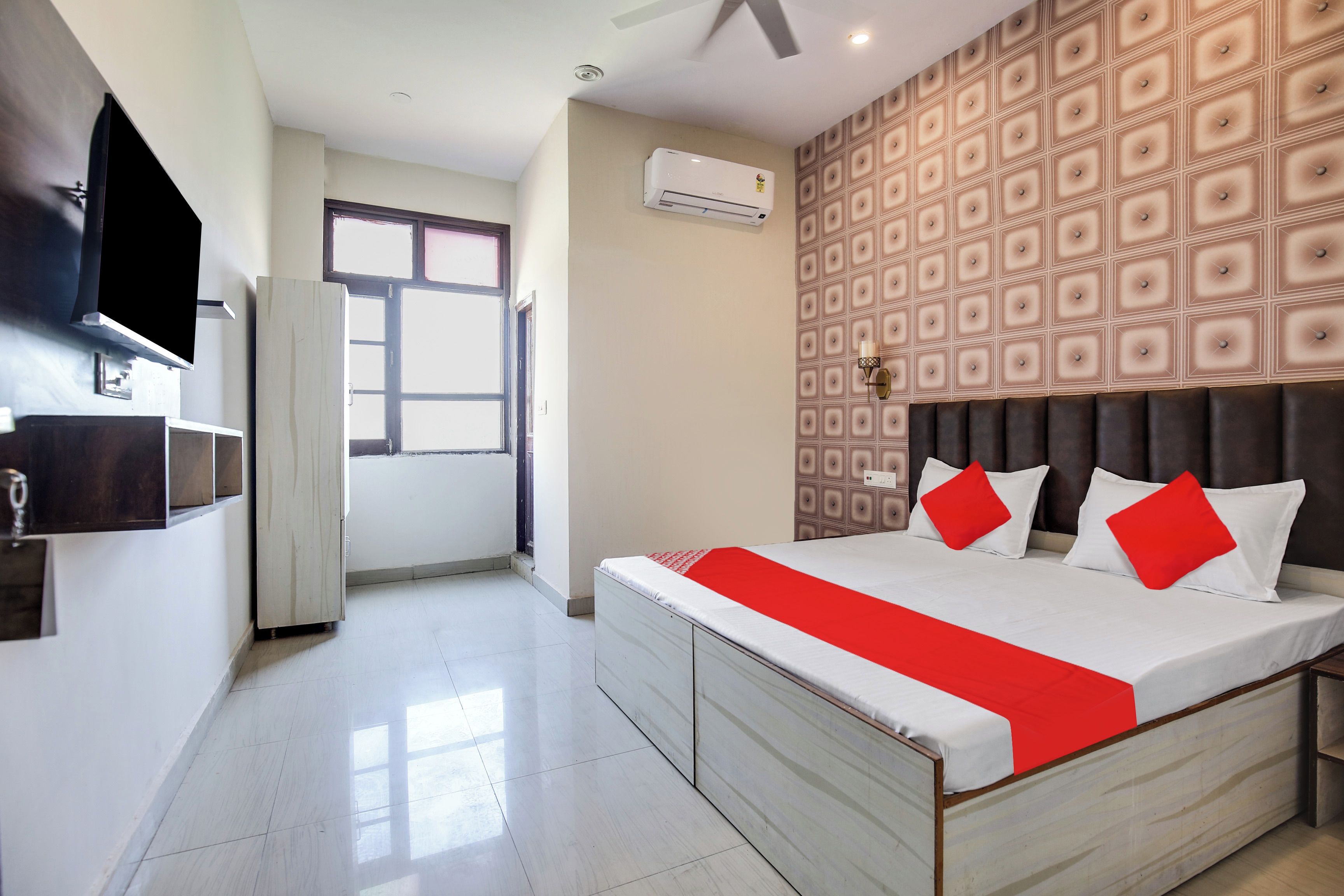 Una habitación de hotel con cama, televisor, aire acondicionado, ventana y pared con diseño.