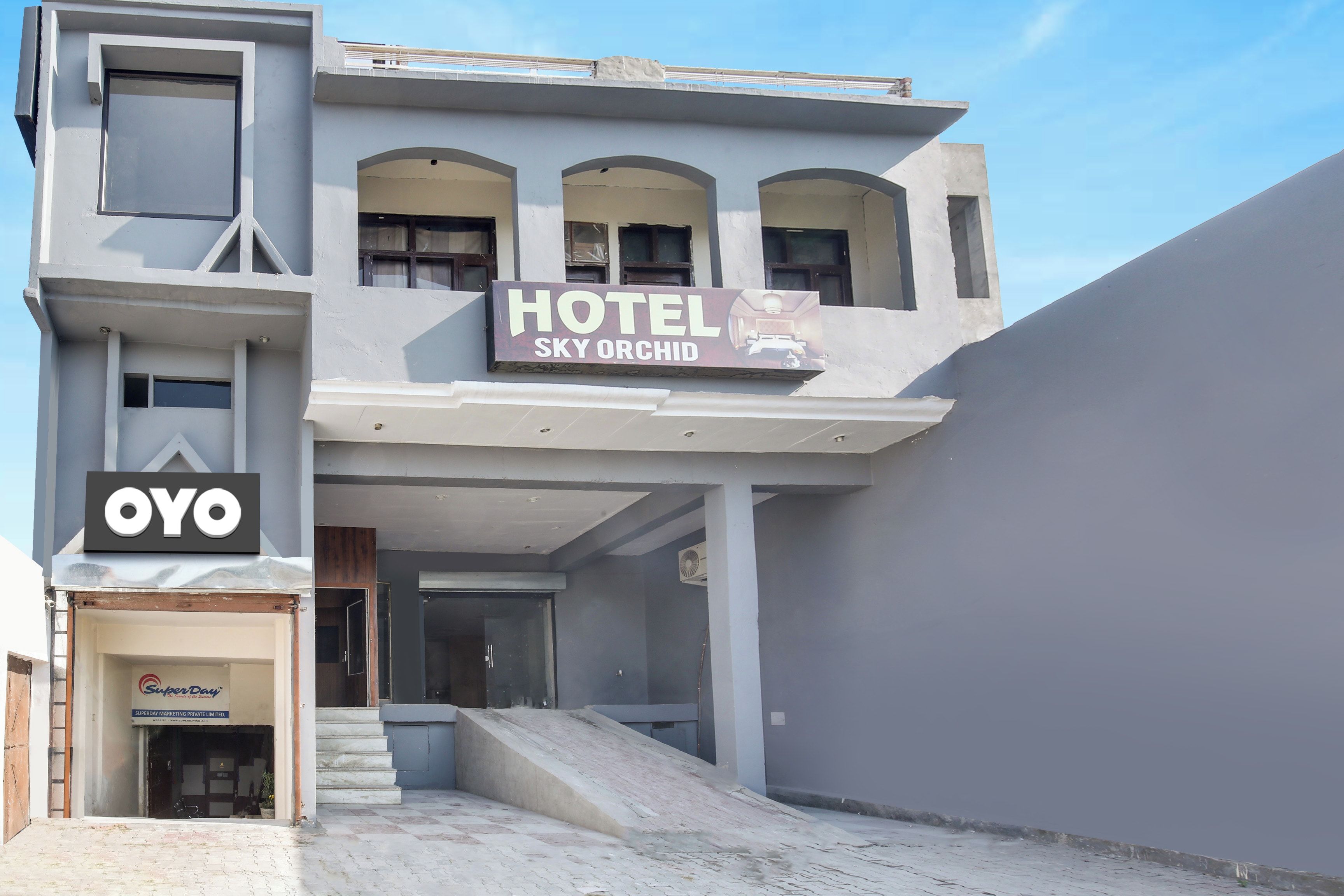 Un hotel llamado 'Hotel Sky Orchid' con un diseño arquitectónico moderno, que cuenta con una entrada destacada con escalones y una señal.