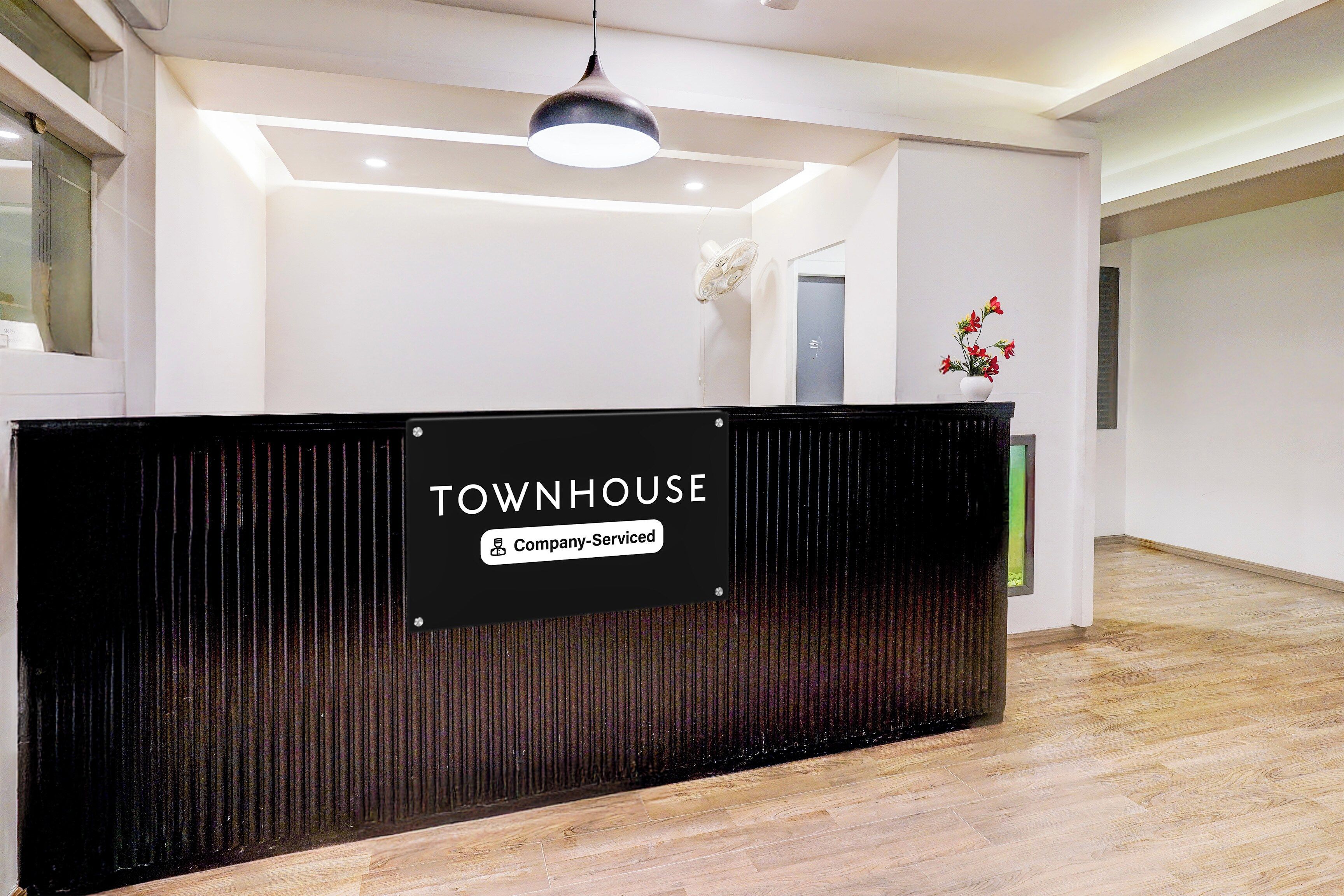 A reception desk with a sign indicating 'Company-Serviced' and a modern interior with a wooden floor and a ceiling light.