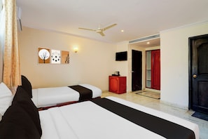 Quarto de hotel com duas camas, ventoinha no teto, TV na parede e obras de arte.