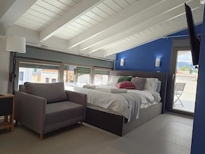 Een slaapkamer met een bed, een bank, een televisie en een raam.