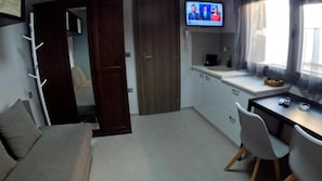 A compact room with a sofa, a dining table with chairs, a television mounted on the wall, and a window with curtains. - Data Maisonettes and More (Chios)