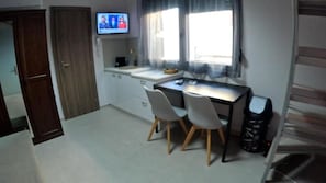 A small room with a desk, two chairs, a television, a window with curtains, and a trash bin. - Data Maisonettes and More (Chios)