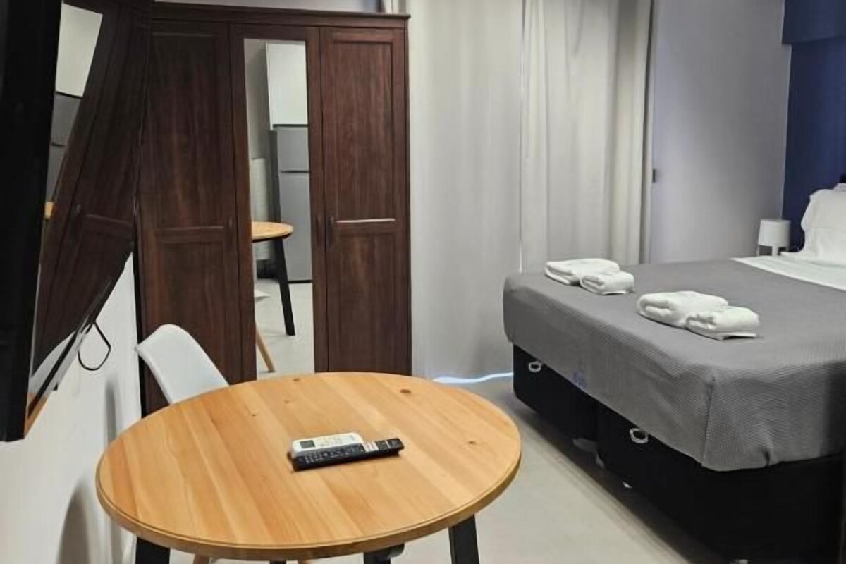 A hotel room with a bed, a small table, a TV, and a wardrobe.