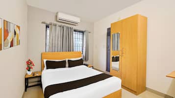 A hotel room with a bed, bedside table, nightstand, an air conditioning unit, a wardrobe, and a window with curtains.