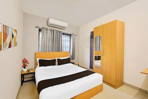 A hotel room with a bed, bedside table, nightstand, an air conditioning unit, a wardrobe, and a window with curtains. - Townhouse Nanganallur Near Chennai (Chennai)