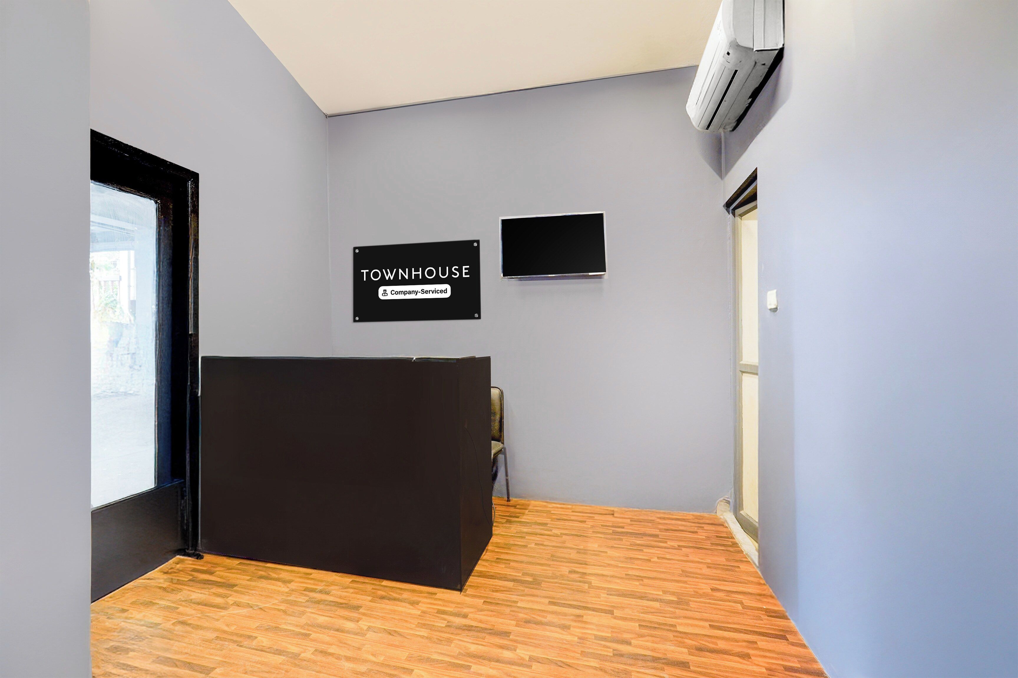 Zona de recepción de un hotel con un mostrador negro, un cartel que indica que es una casa de campo con servicios de empresa, y un televisor de pantalla plana montado en la pared.