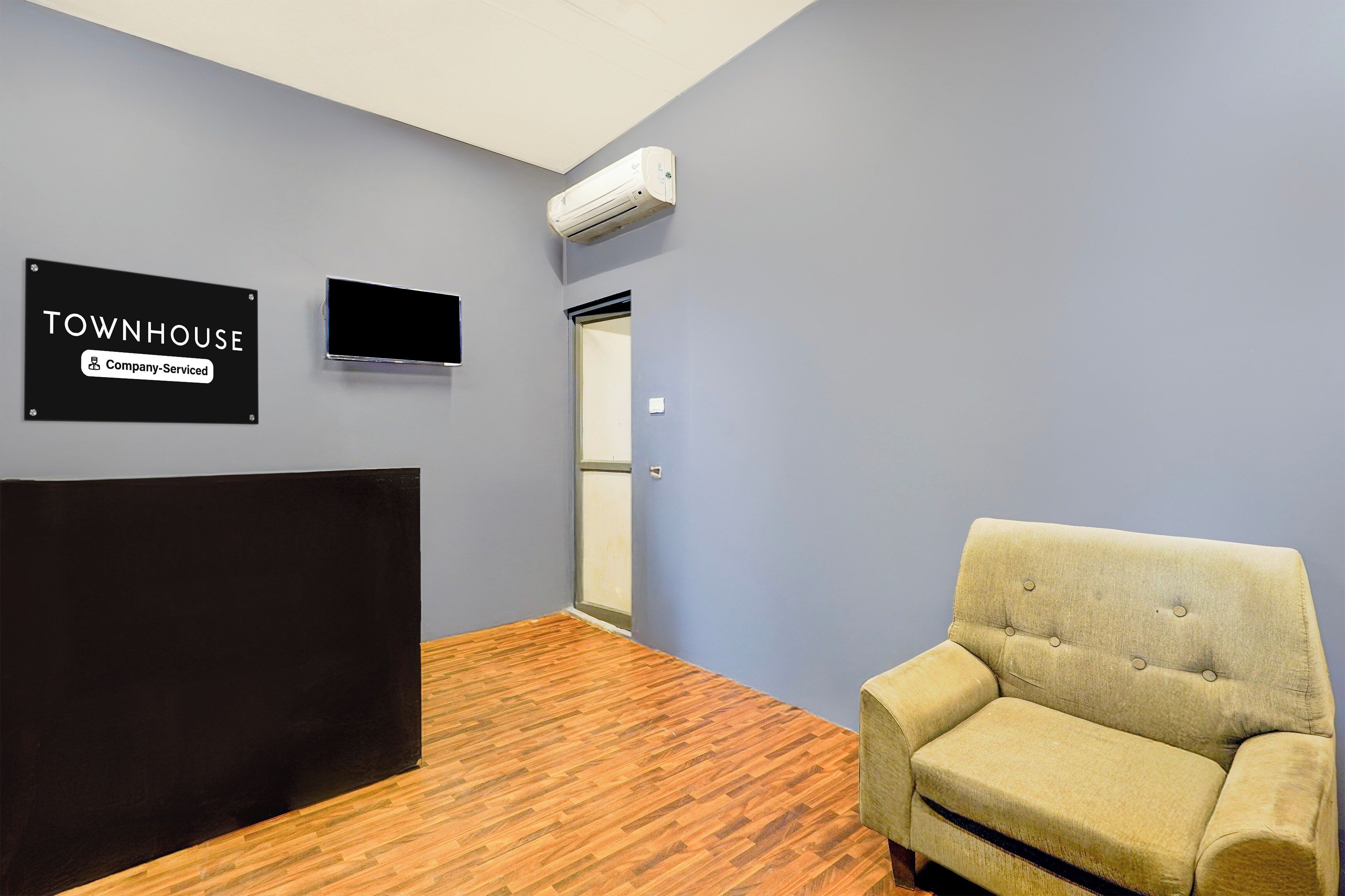 Una habitación con cabecera negra, un sillón beige, un letrero que indica que es una casa townhouse de servicio de empresa, y un equipo de aire acondicionado en la pared.