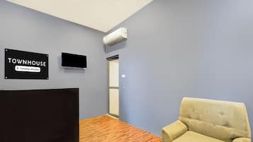 Una habitación con cabecera negra, un sillón beige, un letrero que indica que es una casa townhouse de servicio de empresa, y un equipo de aire acondicionado en la pared.
