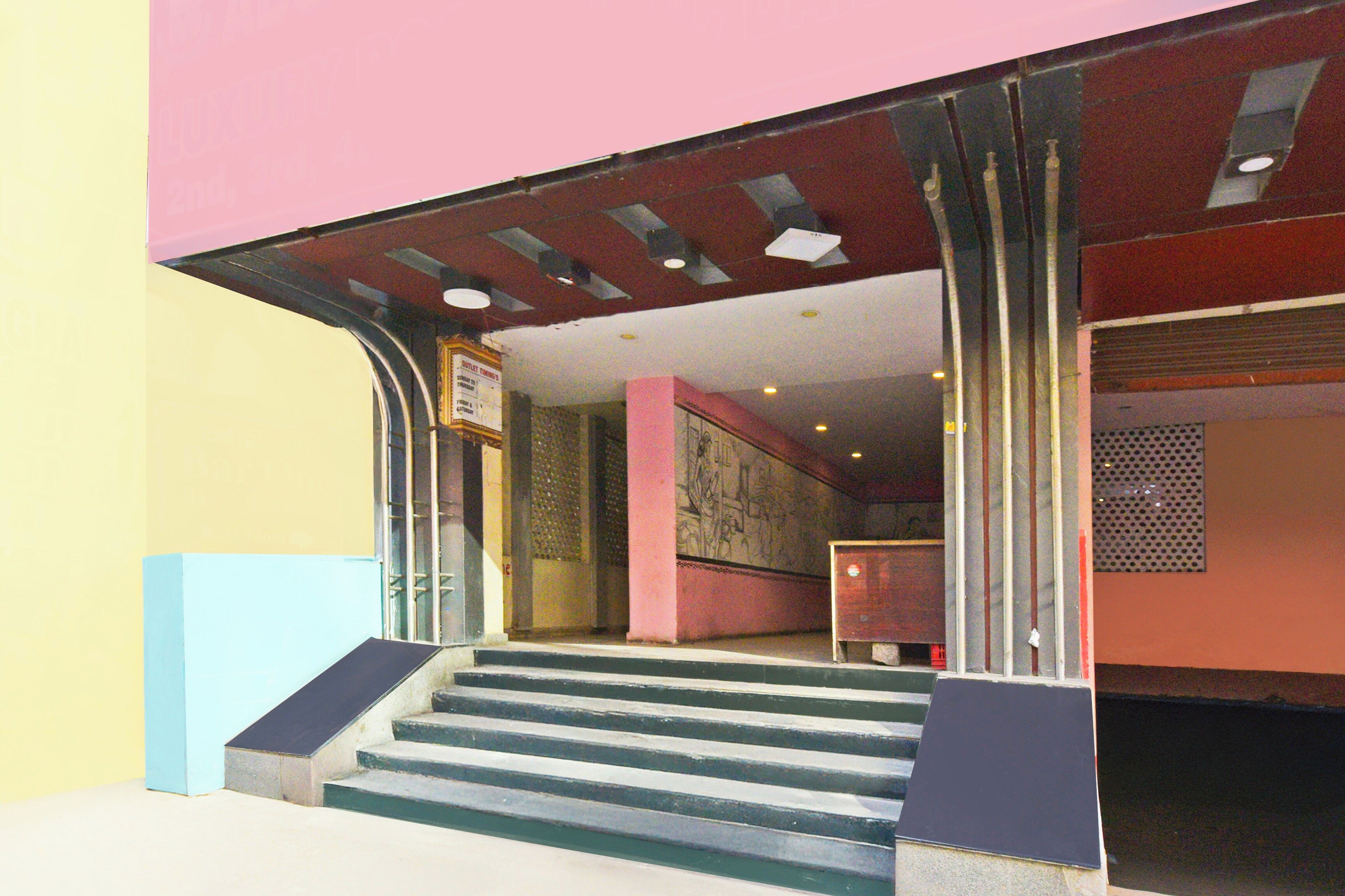 Entrada de un edificio con una escalera que lleva a una puerta, un cartel sobre la puerta y una pared con diseño decorativo.