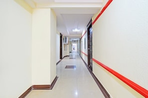 Um corredor comprido e estreito com paredes brancas e uma faixa vermelha na lateral direita.