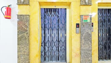 Un ascensor con puerta metálica, un extintor montado en la pared y un cartel que indica los procedimientos de emergencia.