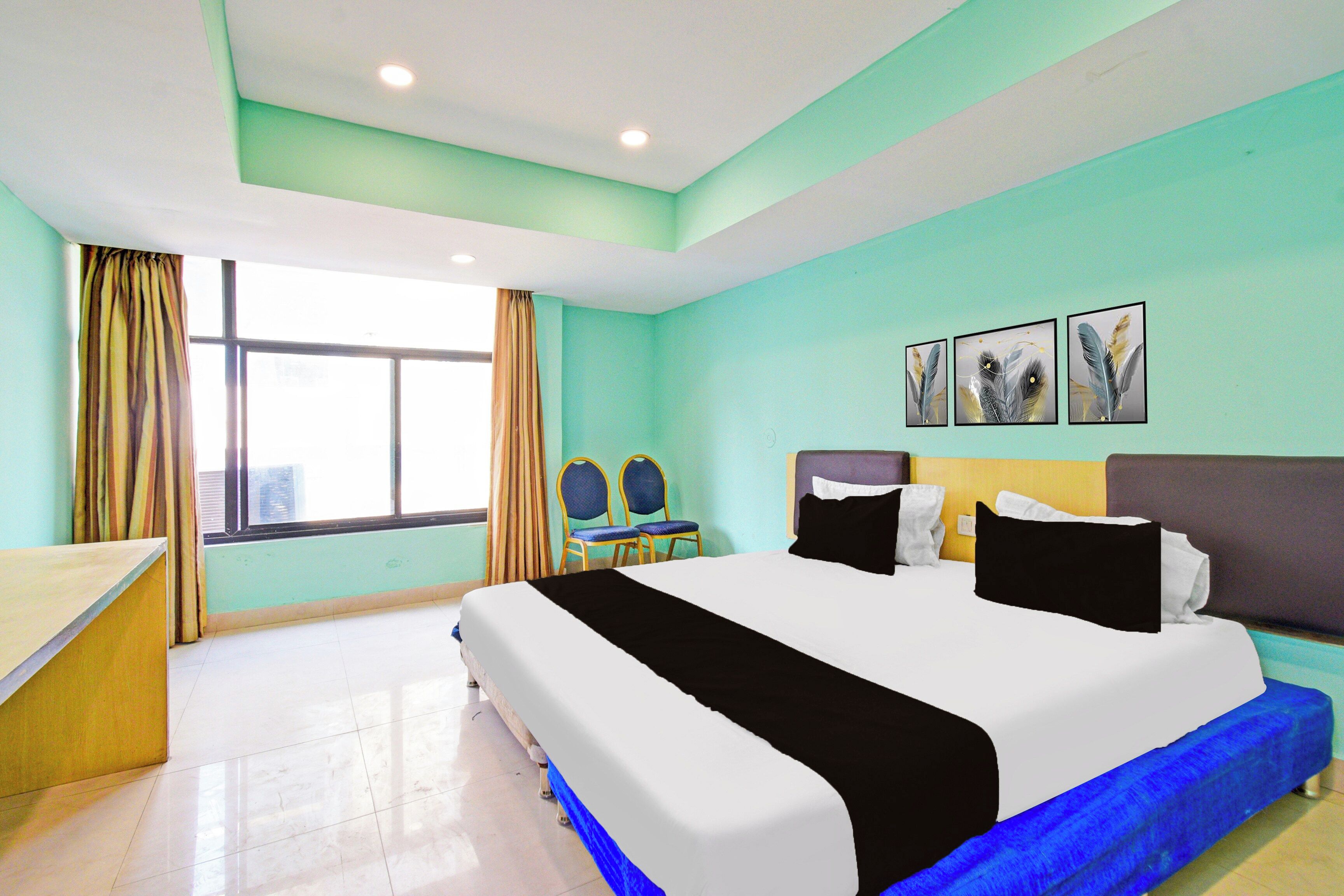 A hotel room with a bed, a desk, a chair, a window with curtains, and wall art.