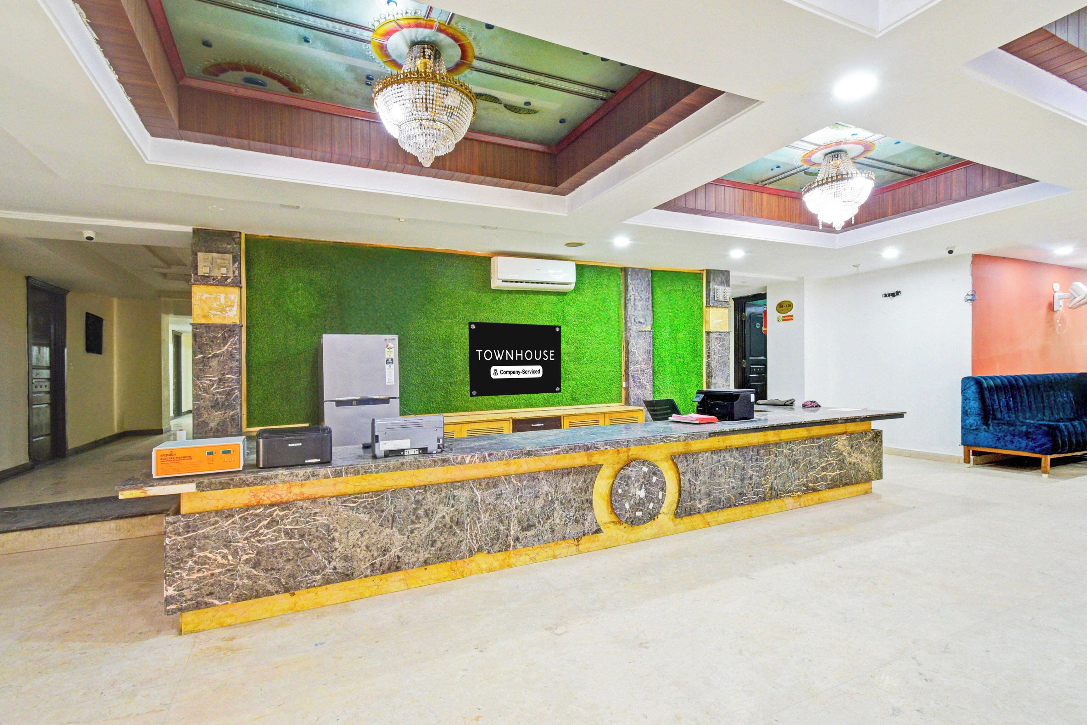 Zona de recepción con pared verde, un letrero que dice 'TOWNHOUSE Company Serviced' y un escritorio negro con una computadora e impresora.
