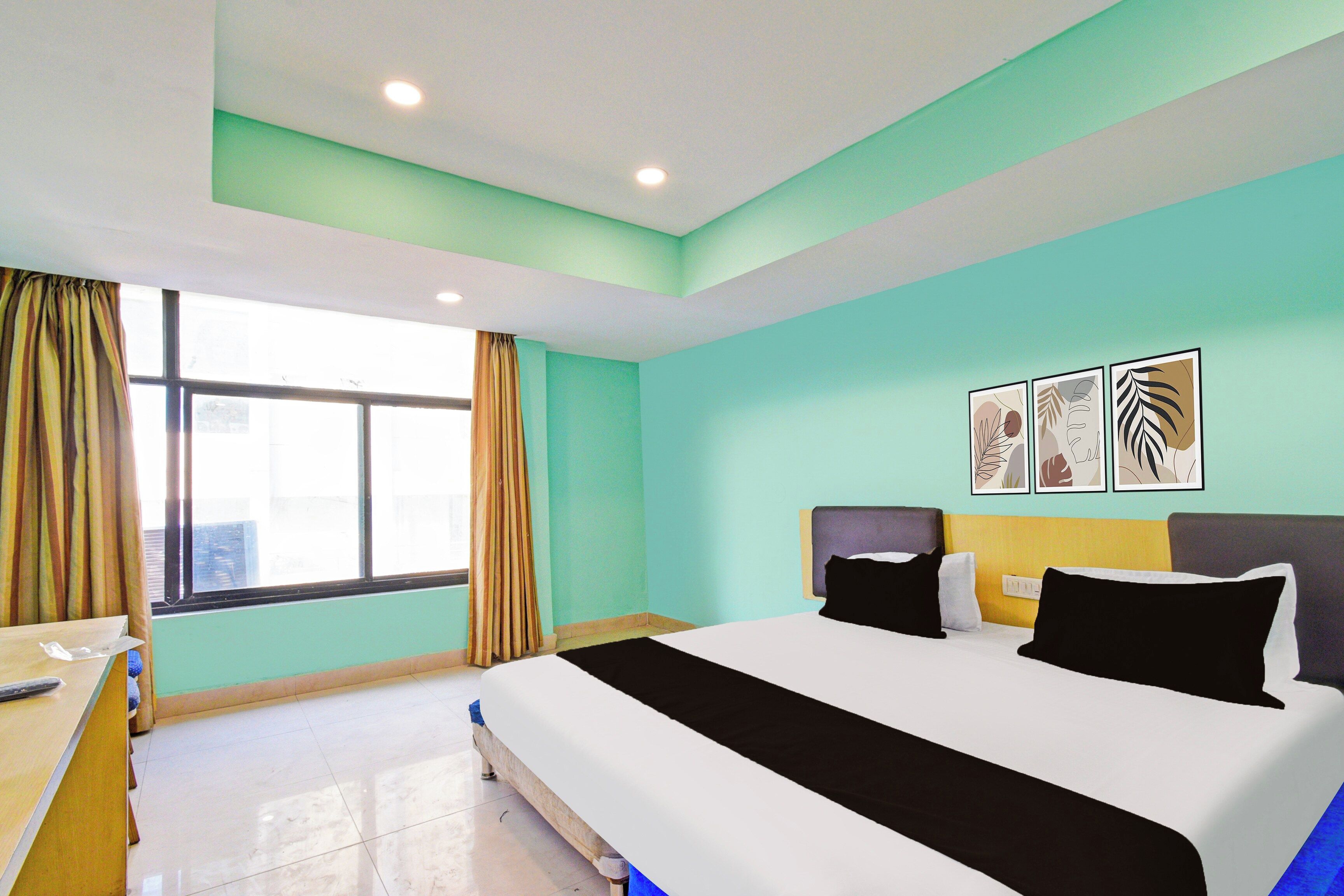 Une chambre d’hôtel avec un lit, un bureau, une fenêtre avec des rideaux et des œuvres d’art murales.