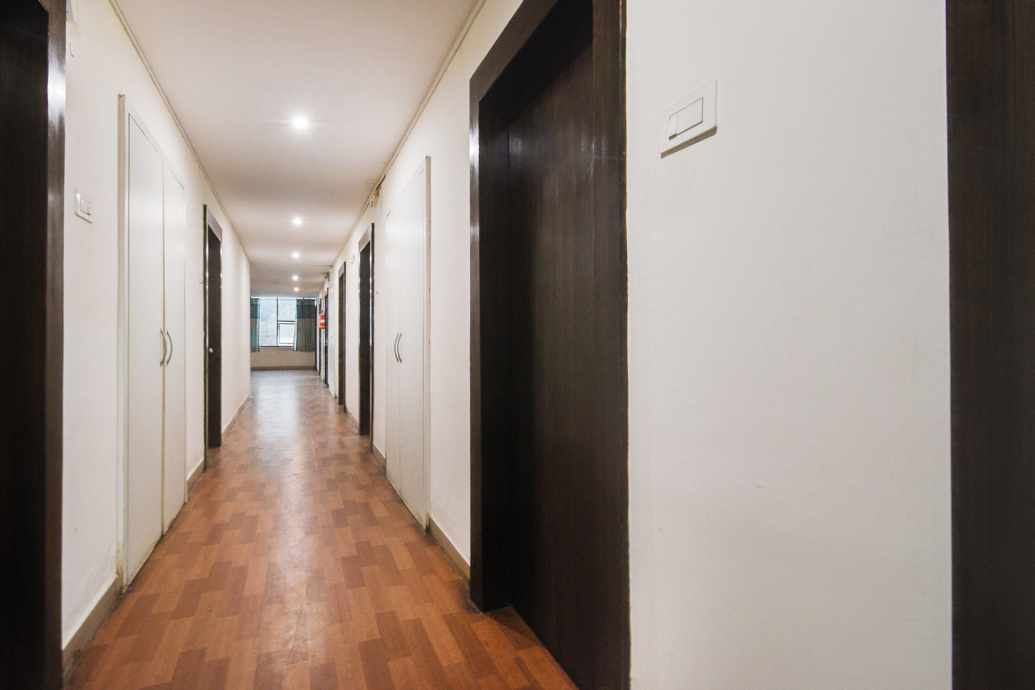 Un passadís llarg i estret amb sòl de fusta i parets blanques, que condueix a una habitació amb un gran finestral.