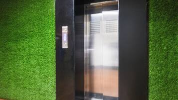 Un ascenseur doté d’un panneau de commande et d’une porte métallique, le tout installé devant un mur vert.