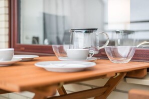 Een houten tafel met een glazen karaf, een witte beker en een schoteltje.
