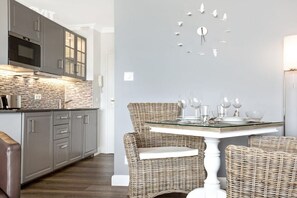 A modern kitchen with grey cabinets, a microwave, and a tiled backsplash. There is a dining area with wicker chairs and a glass table set with wine glasses and plates. - Holiday apartment in Sylt with 1 bedroom (Westerland\/Sylt)