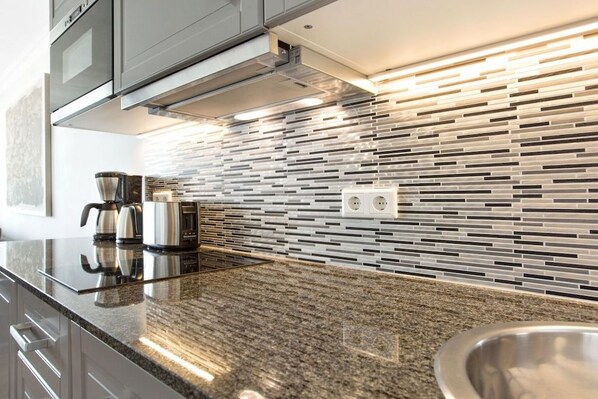 Een moderne keuken met een granieten aanrechtblad, roestvrijstalen apparatuur en een betegelde achterwand.