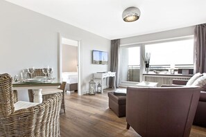 A modern hotel room with a dining area, a sofa, a television, and a view of the city. - Holiday apartment in Sylt with 1 bedroom (Westerland\/Sylt)