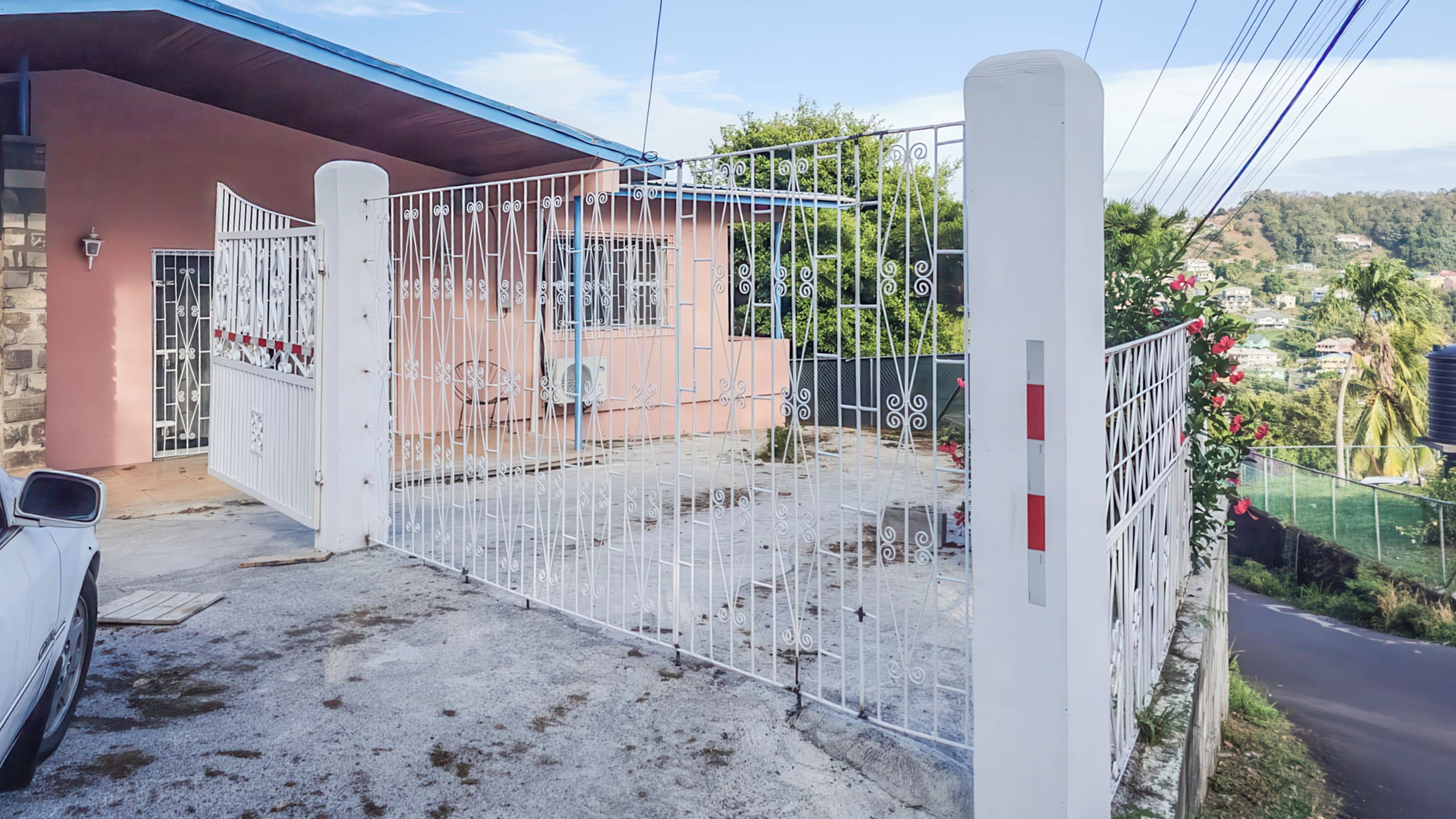 A gated entrance with a white fence, a parked car, and a building with a stone facade.