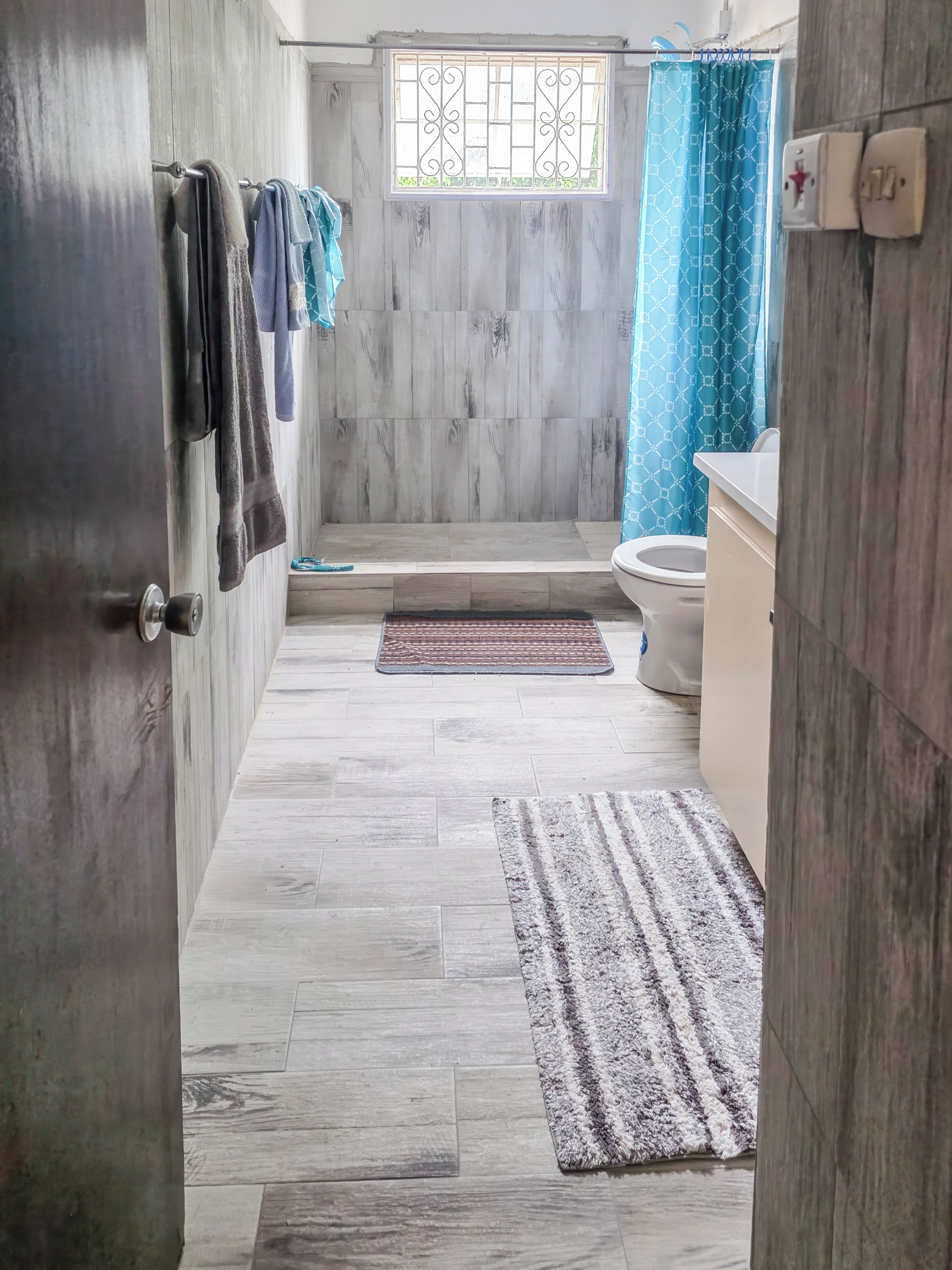 A bathroom with a toilet, a sink, a shower area, and a window with a curtain.
