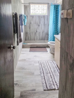A bathroom with a toilet, a sink, a shower area, and a window with a curtain. - Home Away From Home (Arnos Vale)