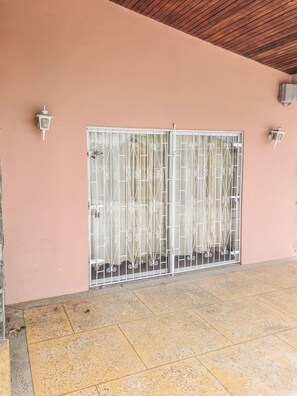 A building with a pink wall, a metal gate with decorative bars, and two wall-mounted light fixtures. - Home Away From Home (Arnos Vale)