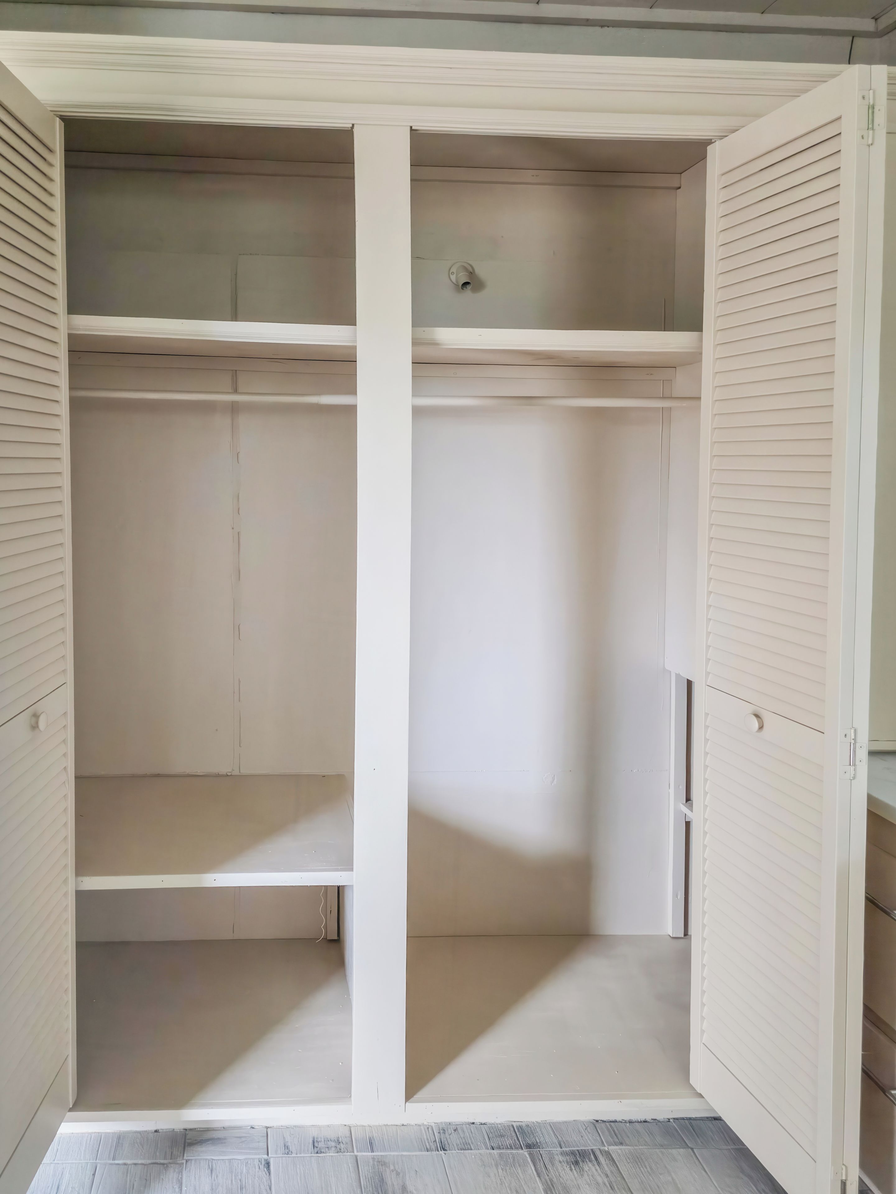Un armario blanco con puertas correderas, un grifo de agua visible y un piso con baldosas.