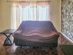 A room with a covered sofa, a small table, and a patterned wall.