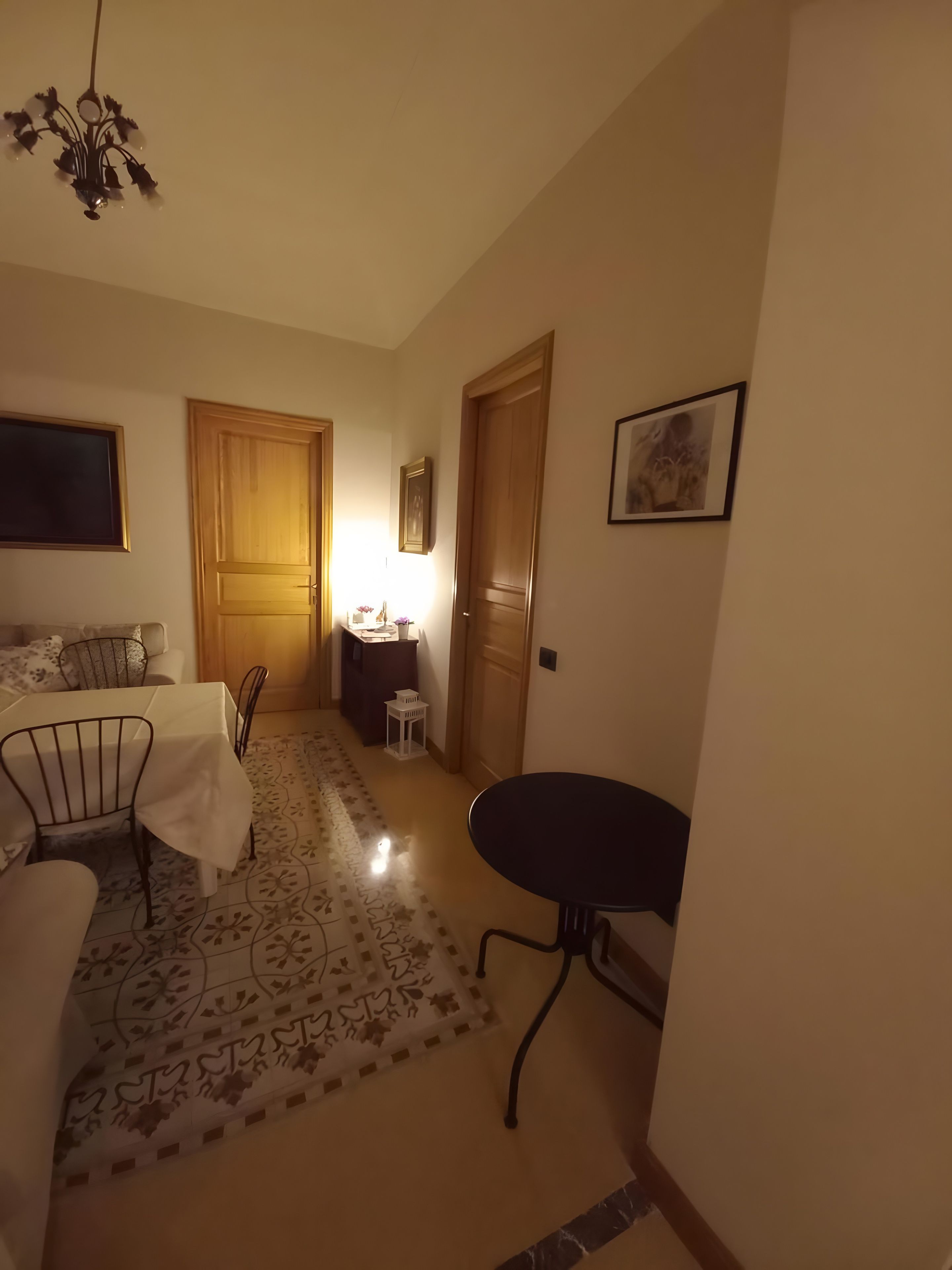 Une pièce comprenant une table à manger, des chaises, une petite table ronde, un lustre, une porte en bois et un tableau encadré accroché au mur.