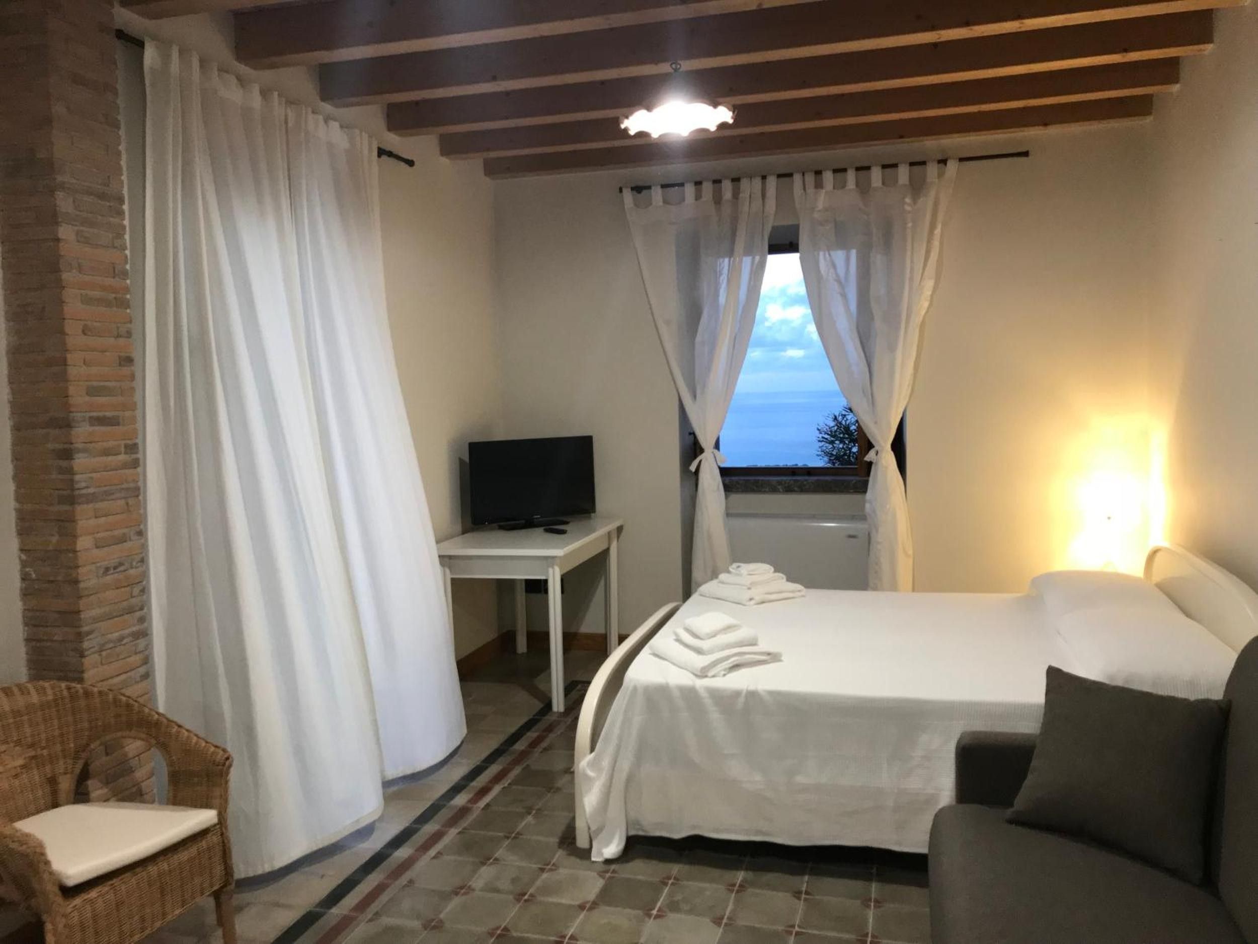Een slaapkamer met een bed, een televisie op een bijzettafeltje, een stoel en een raam met gordijnen.