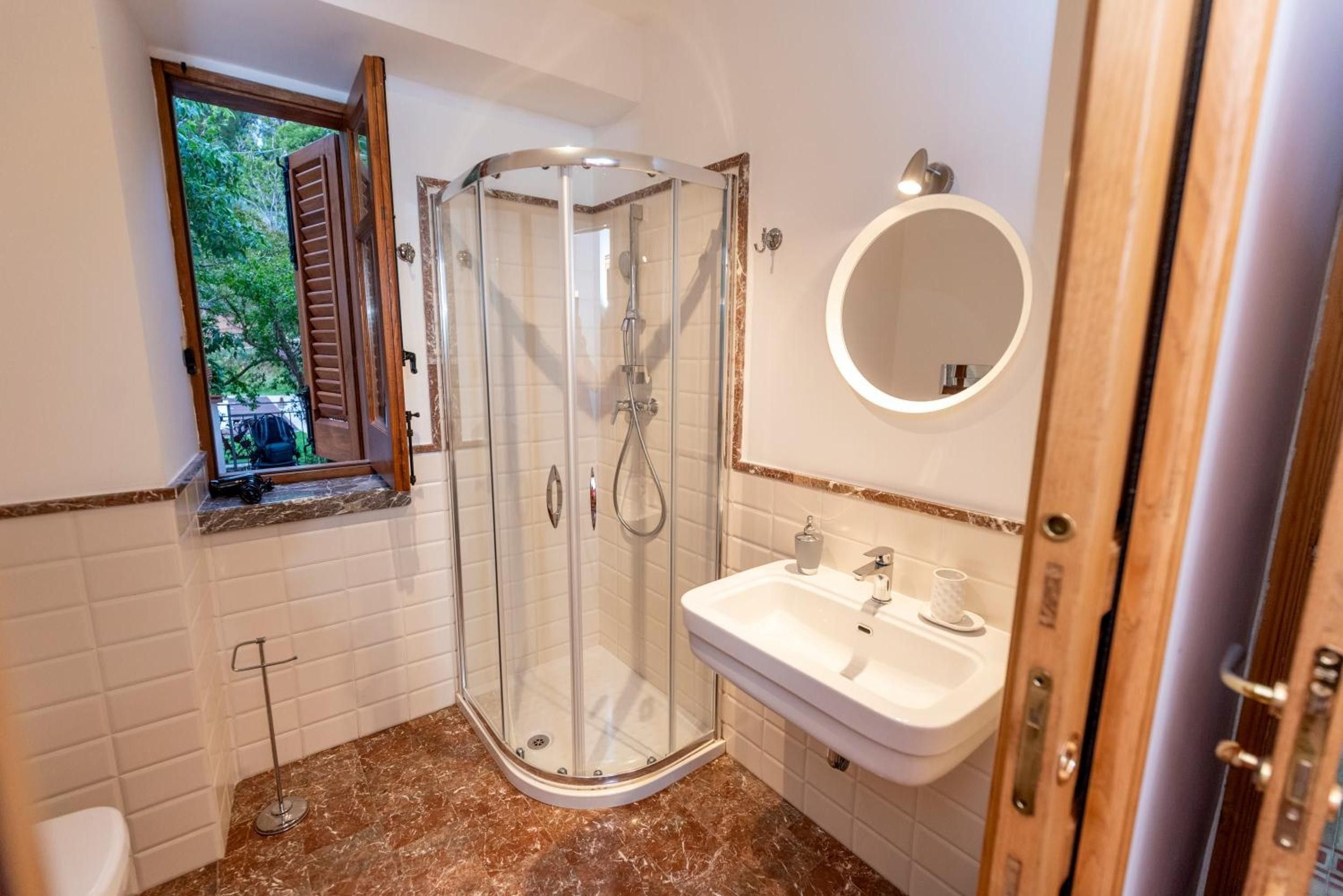 Une salle de bain avec une douche à parois de verre, un lavabo avec un miroir et une fenêtre donnant sur un espace verdoyant.