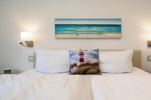 A bed with white bedding, a painting of a beach scene, and two wall-mounted lamps. - Holiday apartment with 2 bedrooms (Westerland - Sylt)