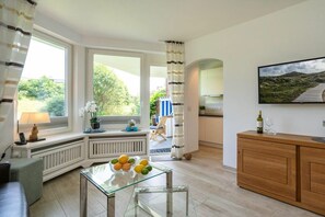 Una sala de estar moderna con una mesa de vidrio, un mueble de madera y un ventanal con cortinas.