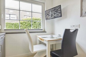 A small dining area with a table, two chairs, a window, and a wall-mounted picture. - New Love - Süderstr. 18c (Sylt)