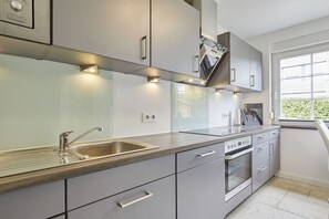A modern kitchen with a stainless steel sink, built-in oven, and grey cabinetry. - New Love - Süderstr. 18c (Sylt)
