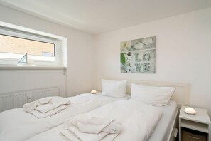 A bedroom with a bed, two bedside lamps, a window with a sailboat decoration, and a wall art piece with the words 'LOVE'. - Sylt Residence Apartment 5 (Sylt Ortsteil Westerland)