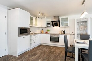 A modern kitchen with white cabinetry, a built-in oven, and a dining area with a table and chairs. - Sylt Residence Apartment 5 (Sylt Ortsteil Westerland)