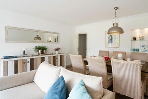 A living room with a sofa, dining table, chairs, a hanging pendant light, and a large mirror. - Ostertresker Sea Garden (Tinnum - Sylt)