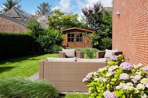 A garden with a wicker sofa, a wooden structure, and a brick wall. - Ostertresker Sea Garden (Tinnum - Sylt)