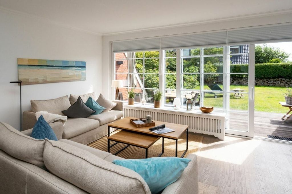 Ein modernes Wohnzimmer mit großem Fenster, einer Couch, einem Couchtisch und einem Gemälde an der Wand.