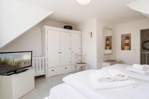 A hotel room with a TV, white wardrobe, two beds, and artwork on the walls. - Ostertresker Sea Garden (Tinnum - Sylt)