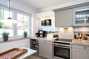 A modern kitchen with a built-in oven, a coffee maker, and a window with plants. - Ostertresker Sea Garden (Tinnum - Sylt)