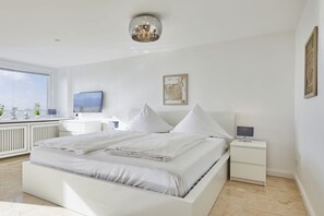Ein modernes Schlafzimmer mit einem großen Bett, Nachttischen, einem Fernseher und Kunstwerken an der Wand.