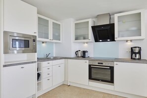 Eine kompakte Küche mit weißen Schränken, einer eingebauten Mikrowelle, einer Kaffeemaschine und einem Toaster.