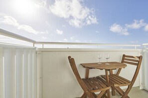 Ein Holztisch und -stühle auf einem Balkon mit weißer Brüstung und blauem Himmel.
