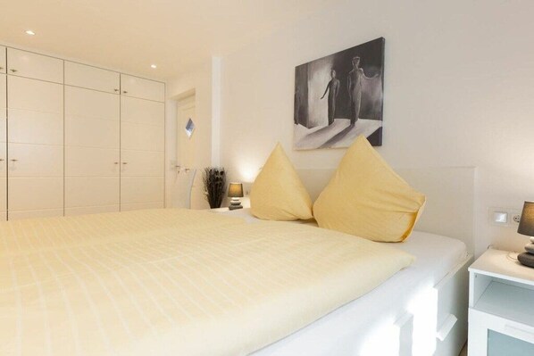 Quarto com cama grande, guarda-roupa, mesa de cabeceira e uma obra de arte na parede.